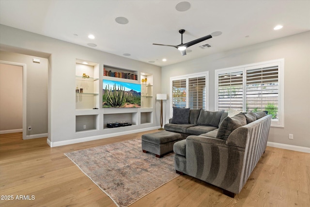 living area with built in features, ceiling fan, light wood-type flooring, visible vents, and baseboards