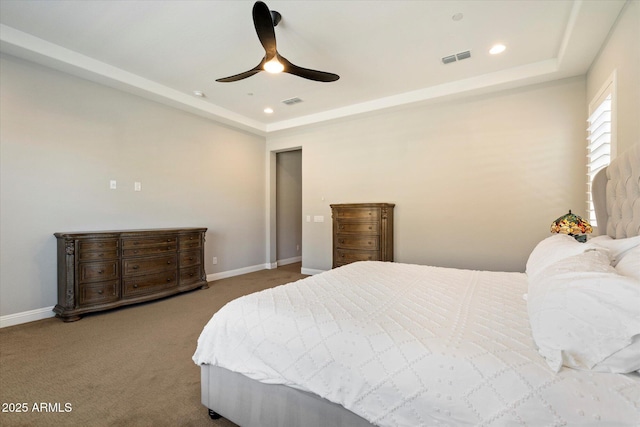 carpeted bedroom with a tray ceiling, baseboards, and visible vents