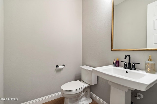 bathroom with toilet, baseboards, and wood finished floors
