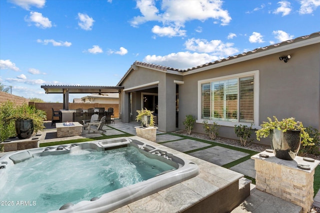 rear view of property with a patio, stucco siding, an outdoor hot tub, an outdoor fire pit, and fence