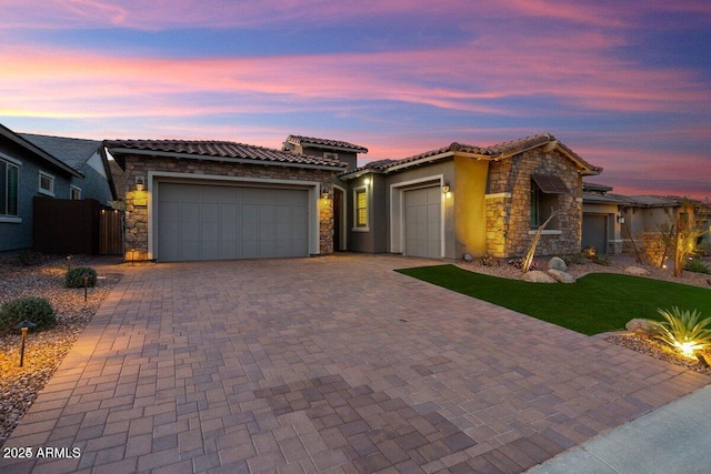 view of front of home featuring a tiled roof, a garage, stucco siding, stone siding, and driveway
