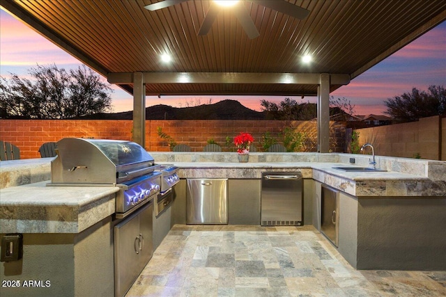 patio terrace at dusk with grilling area, area for grilling, a fenced backyard, and a sink