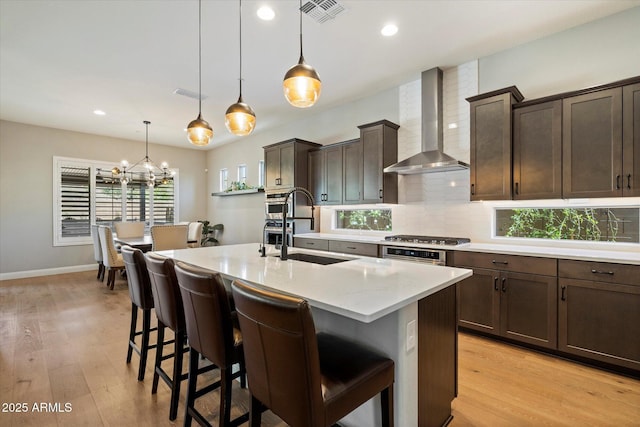 kitchen with wall chimney range hood, visible vents, a sink, a breakfast bar area, and backsplash