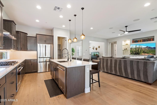 kitchen with light wood-type flooring, open floor plan, dark brown cabinets, stainless steel appliances, and a sink