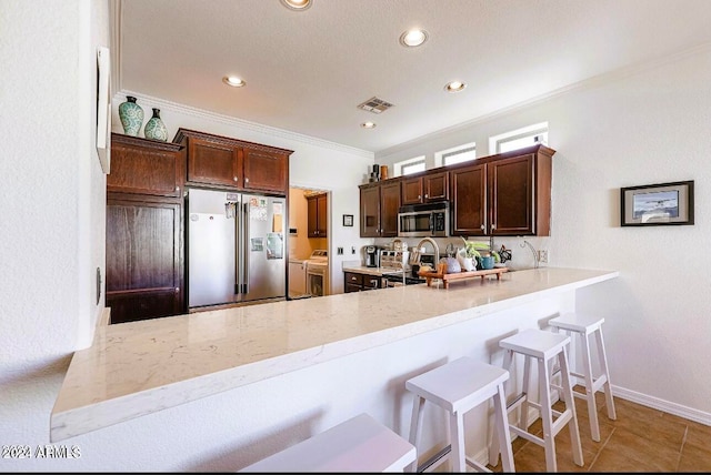 kitchen featuring kitchen peninsula, appliances with stainless steel finishes, crown molding, a breakfast bar area, and light tile patterned flooring