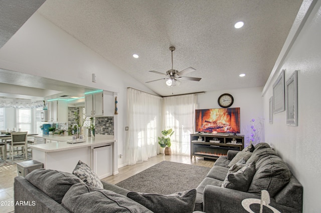 living room with light hardwood / wood-style floors, ceiling fan, vaulted ceiling, a textured ceiling, and sink