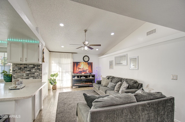 living room with a textured ceiling, ceiling fan, lofted ceiling, and light hardwood / wood-style floors