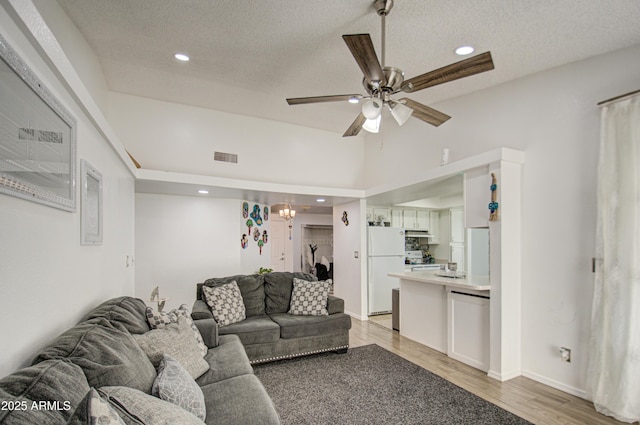 living room with a textured ceiling, ceiling fan with notable chandelier, and light hardwood / wood-style floors