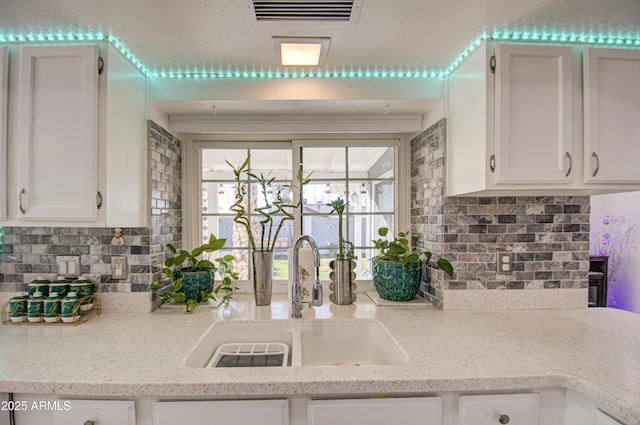 kitchen with light stone counters, sink, white cabinetry, and tasteful backsplash