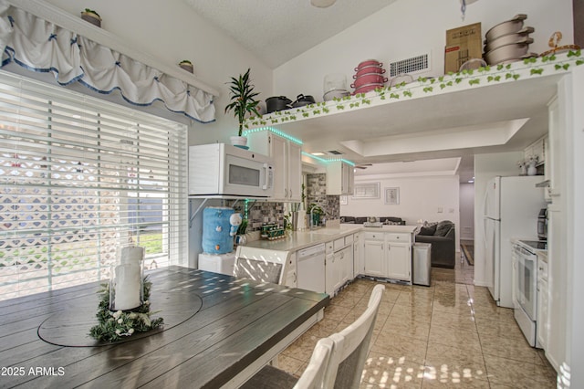 kitchen with a raised ceiling, white appliances, a textured ceiling, white cabinets, and sink