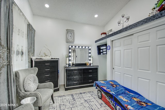 bedroom with lofted ceiling, light tile patterned floors, a closet, and a textured ceiling