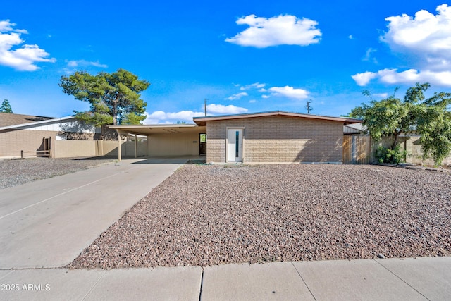 view of front of house with concrete driveway, an attached carport, brick siding, and fence