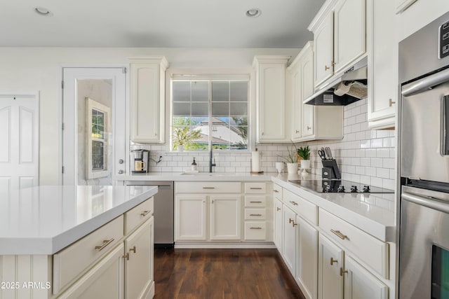 kitchen with appliances with stainless steel finishes, light countertops, under cabinet range hood, and dark wood-type flooring