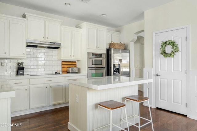 kitchen featuring arched walkways, white cabinets, appliances with stainless steel finishes, dark wood-type flooring, and under cabinet range hood