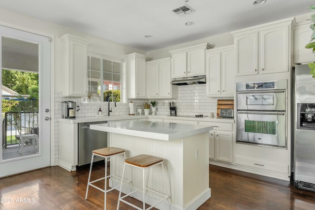 kitchen with white cabinets, dark wood finished floors, appliances with stainless steel finishes, light countertops, and under cabinet range hood