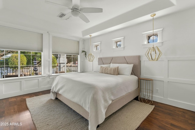 bedroom with ceiling fan, wood finished floors, visible vents, and a decorative wall