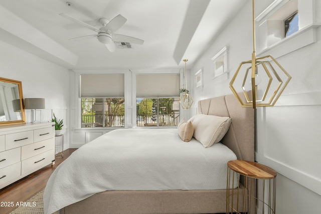 bedroom featuring visible vents, a ceiling fan, a wainscoted wall, dark wood-style flooring, and a decorative wall