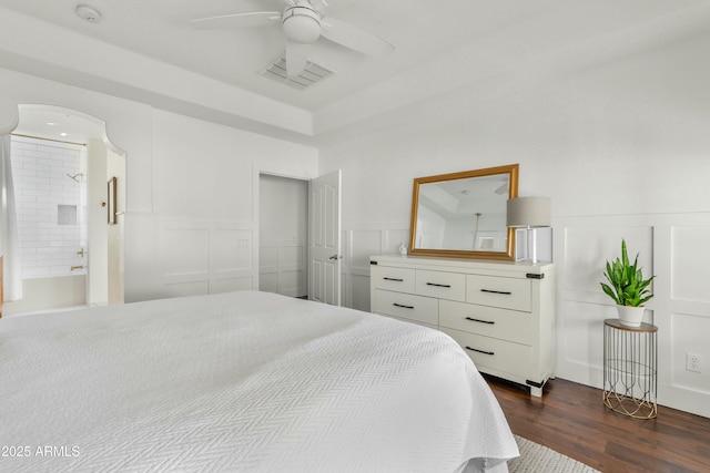 bedroom featuring visible vents, a ceiling fan, dark wood-style floors, ensuite bathroom, and a decorative wall