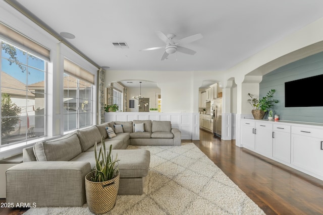 living area featuring ceiling fan, visible vents, arched walkways, and dark wood finished floors