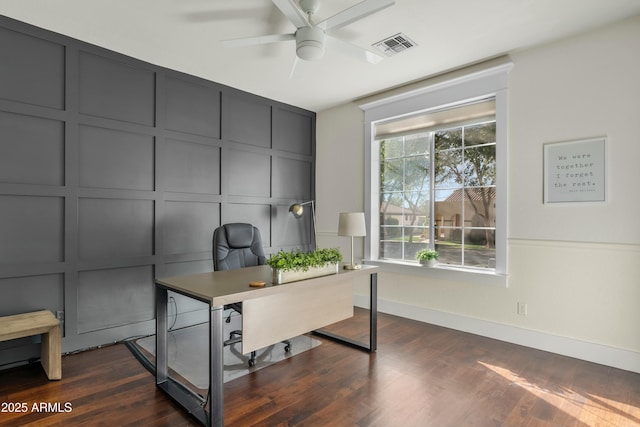 office area featuring dark wood-type flooring, visible vents, a decorative wall, and a ceiling fan