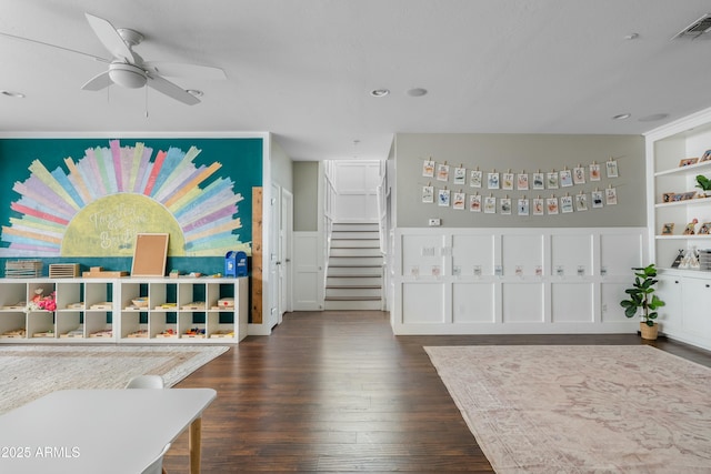 living area featuring built in shelves, visible vents, a ceiling fan, stairs, and dark wood finished floors