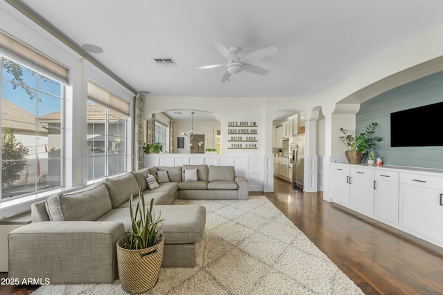 living room with ceiling fan, dark wood-style flooring, arched walkways, and visible vents