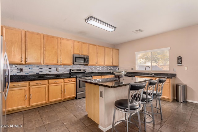 kitchen with a kitchen bar, sink, a center island, appliances with stainless steel finishes, and dark stone counters