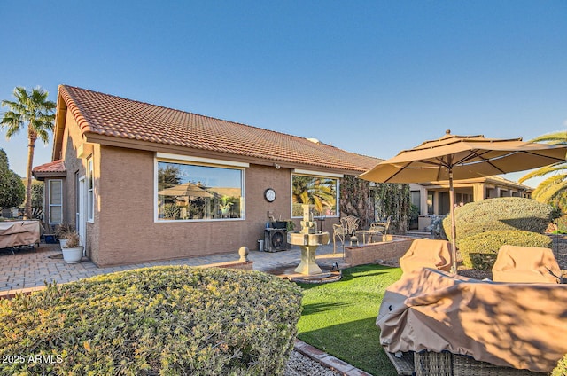 back of house with a patio area, a lawn, a tiled roof, and stucco siding