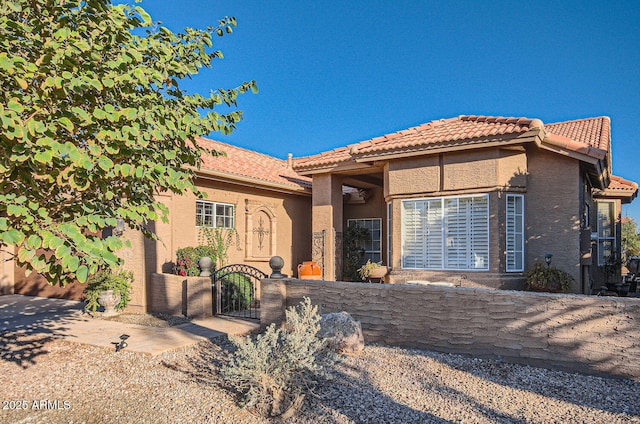 mediterranean / spanish home featuring a tiled roof, a gate, and stucco siding