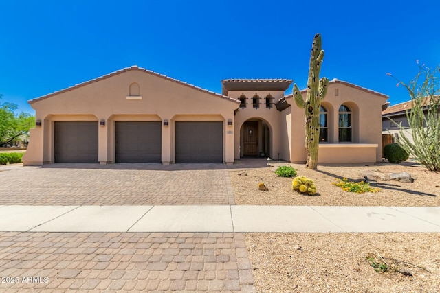 mediterranean / spanish house featuring stucco siding, decorative driveway, an attached garage, and a tile roof