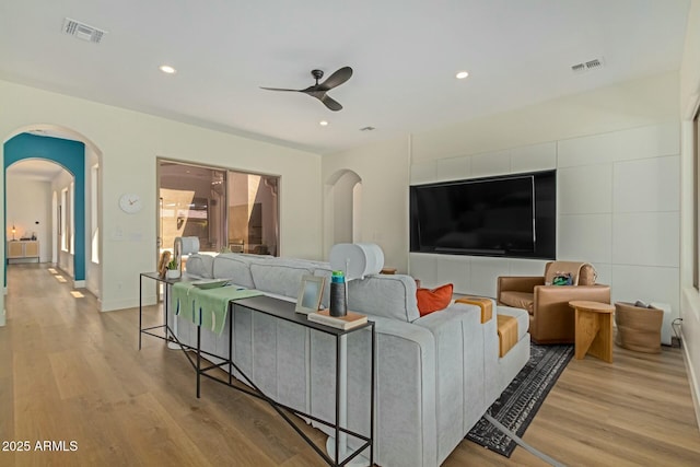 living room featuring ceiling fan, light wood-type flooring, arched walkways, recessed lighting, and baseboards