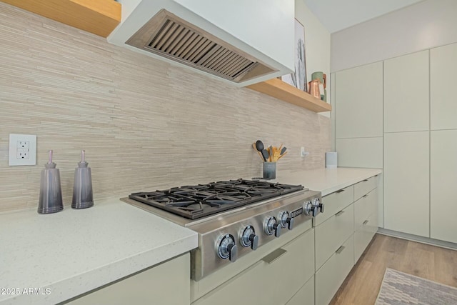 kitchen with ventilation hood, stainless steel gas cooktop, open shelves, and tasteful backsplash