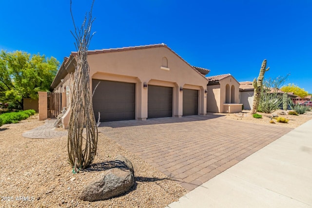pueblo revival-style home featuring stucco siding, decorative driveway, an attached garage, and a tiled roof