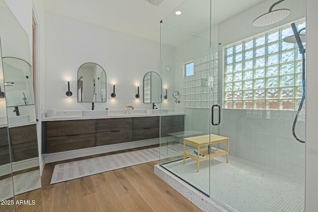 bathroom with wood finished floors, a shower stall, double vanity, and recessed lighting