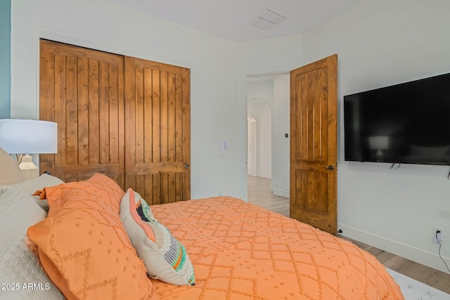 bedroom featuring wood finished floors, baseboards, a closet, and arched walkways
