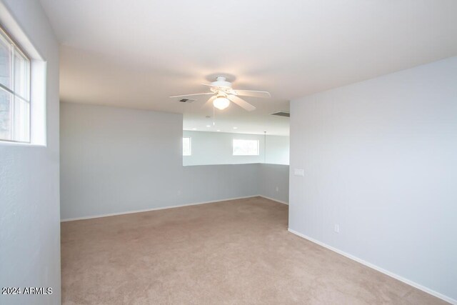 empty room with a wealth of natural light, light carpet, and ceiling fan