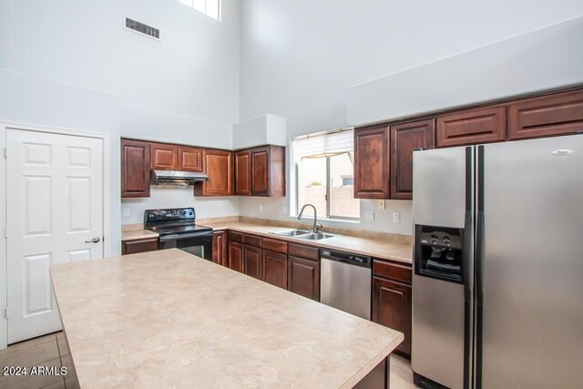 kitchen with a towering ceiling, appliances with stainless steel finishes, sink, a center island, and light tile patterned flooring