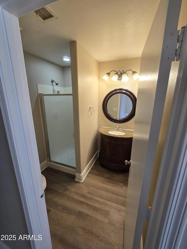 bathroom with toilet, a shower with shower door, a textured ceiling, vanity, and hardwood / wood-style floors