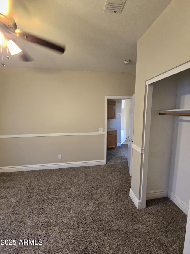 unfurnished bedroom with ceiling fan, a closet, and dark colored carpet