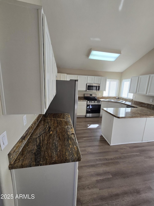 kitchen featuring dark wood-type flooring, appliances with stainless steel finishes, kitchen peninsula, dark stone counters, and white cabinets