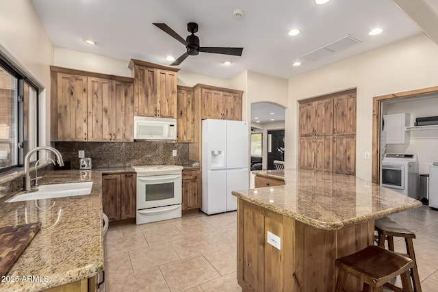 kitchen with light stone counters, arched walkways, visible vents, a sink, and white appliances