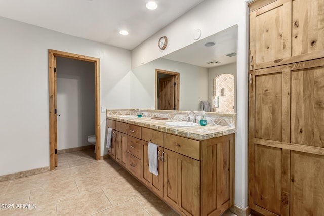 full bathroom with toilet, double vanity, a sink, and tile patterned floors