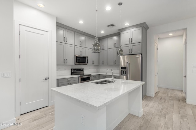 kitchen featuring light stone countertops, appliances with stainless steel finishes, sink, a center island with sink, and hanging light fixtures