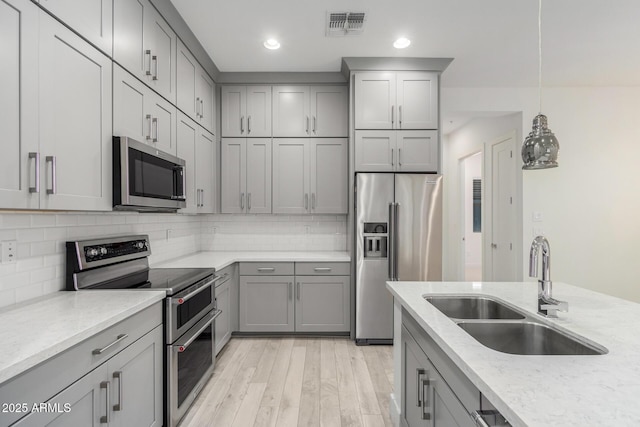 kitchen with pendant lighting, backsplash, sink, light stone countertops, and stainless steel appliances