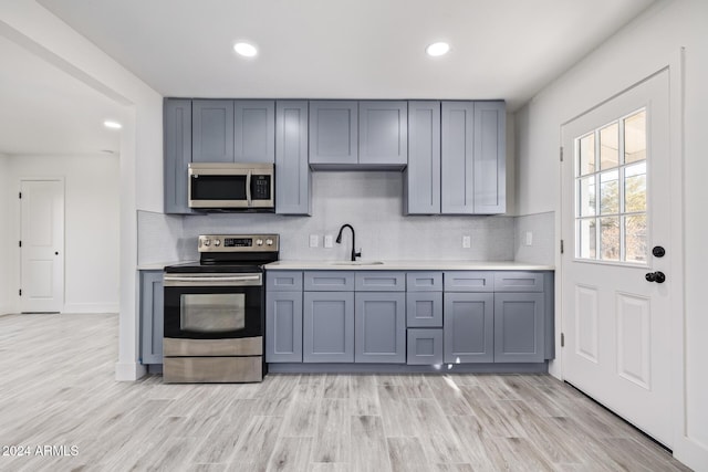 kitchen featuring sink, stainless steel appliances, light hardwood / wood-style flooring, backsplash, and gray cabinets