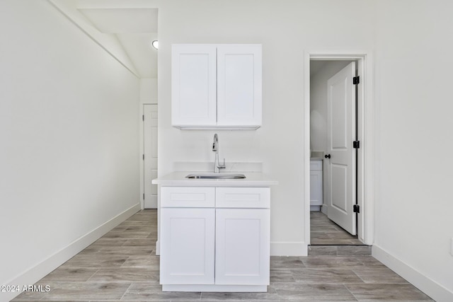 bar with white cabinets, light hardwood / wood-style floors, and sink