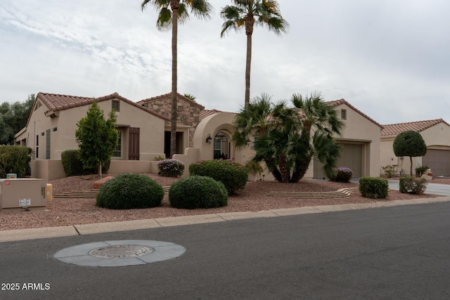 mediterranean / spanish home featuring stone siding, an attached garage, a tile roof, and stucco siding