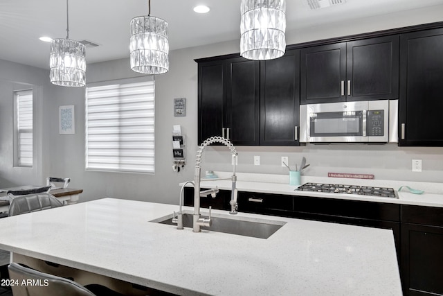 kitchen featuring a wealth of natural light, sink, hanging light fixtures, stainless steel appliances, and light stone counters