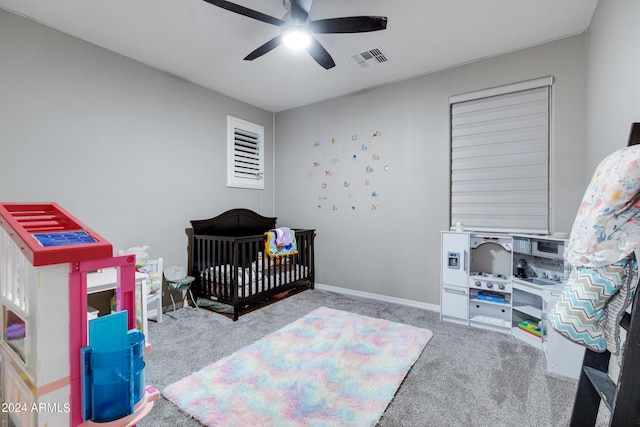 carpeted bedroom featuring ceiling fan and a crib