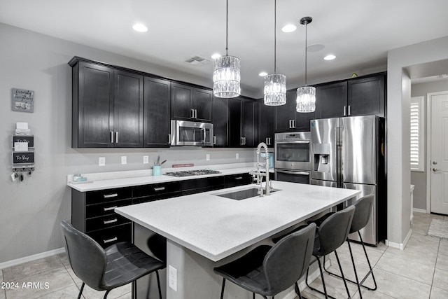 kitchen with a kitchen breakfast bar, stainless steel appliances, a kitchen island with sink, sink, and hanging light fixtures